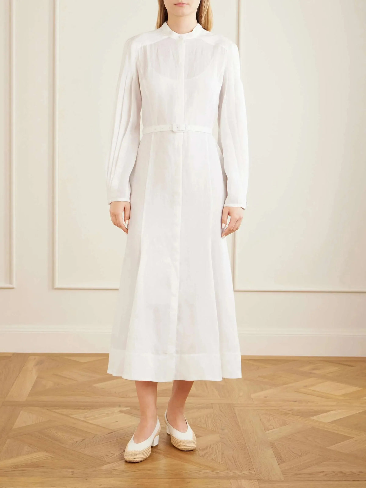Front view of a model wearing a white belted linen midi dress with mandarin collar, button placket and billowed sleeves