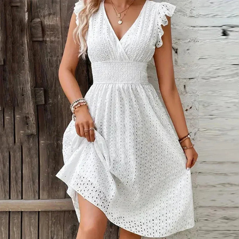 Front view of a white broderie anglaise midi dress with wrap V-neckline, smocked waist and ruffle sleeves
