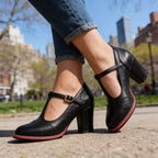 Side view of black leather T-strap brogue heels with wingtip perforated toe and gold buckle