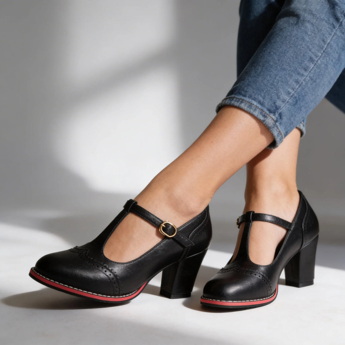 Pair of black T-strap brogue pumps with red contrast sole on model walking on pavement