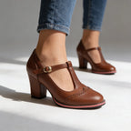 Brown T-strap heeled brogues with perforated detailing shown mid-step on a studio floor