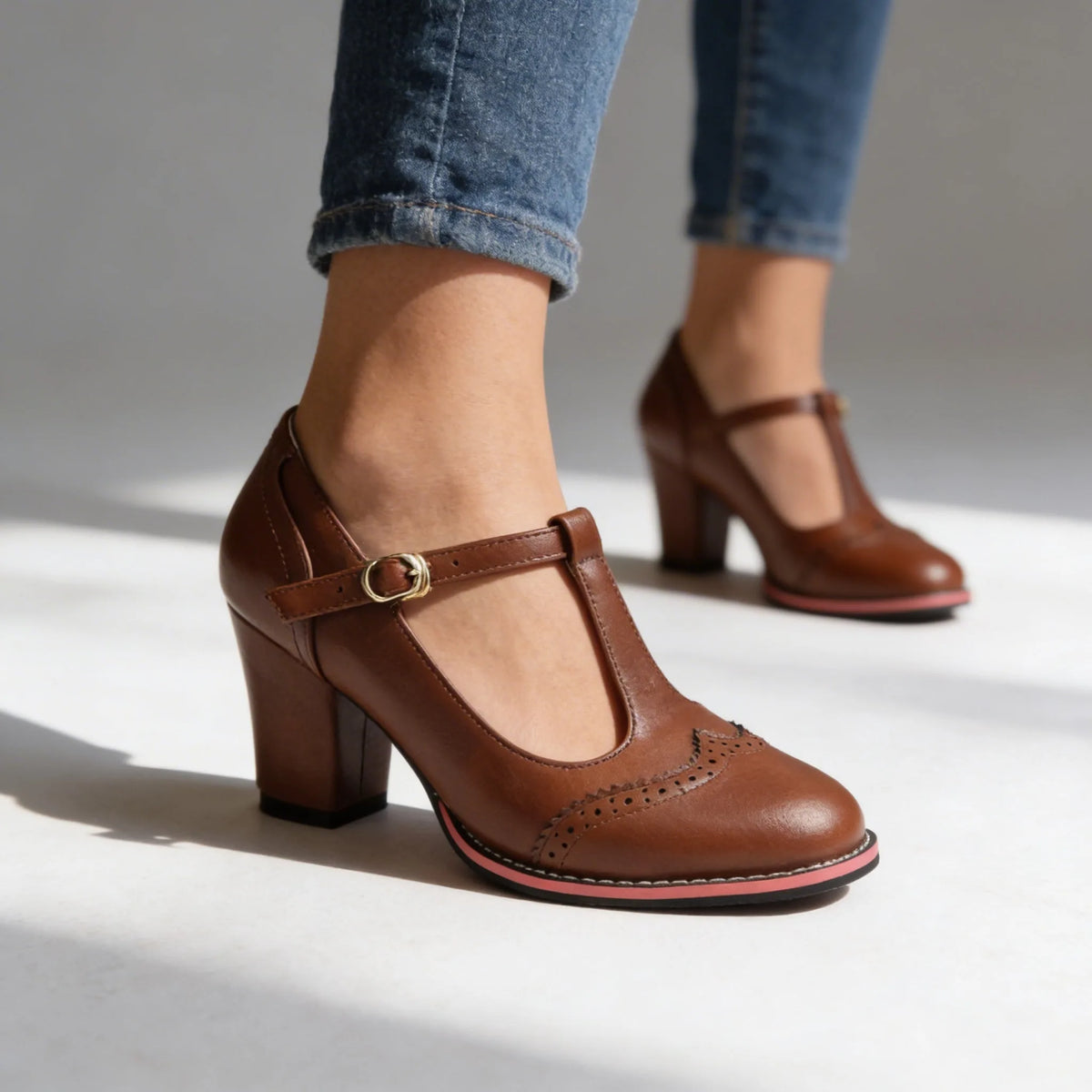 Brown T-strap heeled brogues with perforated detailing shown mid-step on a studio floor