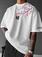 Front view of man wearing white oversized tee with pink cherry blossom branch print and black kanji character near the collar