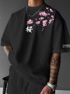 Close-up front view of black oversized tee with pink cherry blossom branch and white kanji character below the shoulder