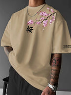 Front view of man wearing khaki oversized tee with pink cherry blossom branch print and black kanji character on the chest