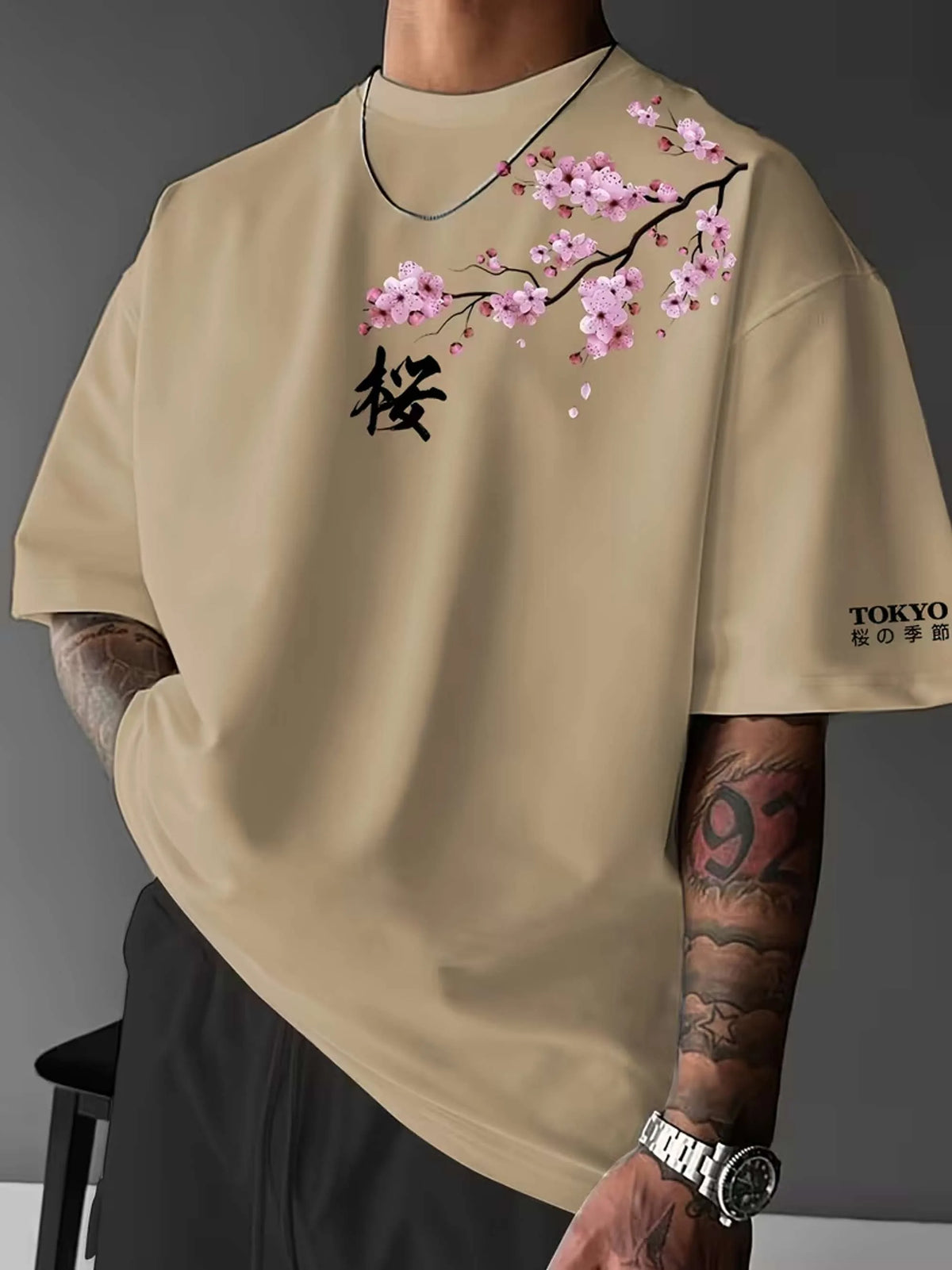 Front view of man wearing khaki oversized tee with pink cherry blossom branch print and black kanji character on the chest