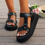 Hand holding a metallic multicolour platform sandal to show the adjustable Velcro closure
