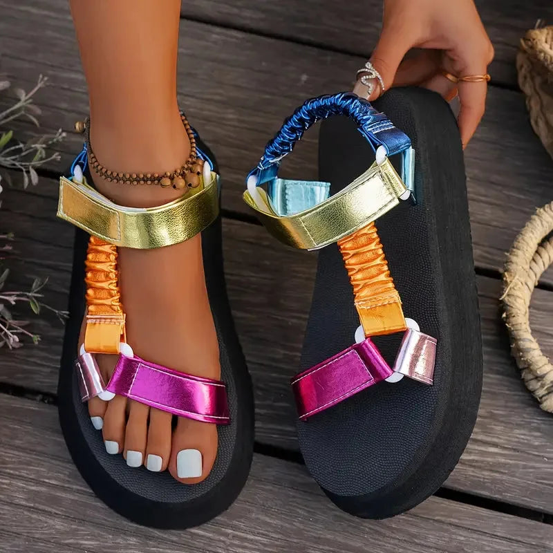 Front view of feet crossed wearing metallic multicolour platform sandals near fresh flowers