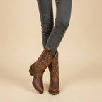 Front view of brown leather pull-on western boots with scalloped shaft and tonal stitching, worn with grey skinny jeans