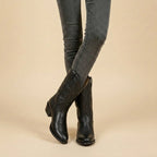 Front view of black leather pull-on western boots with scalloped shaft and tonal stitching, worn with grey skinny jeans
