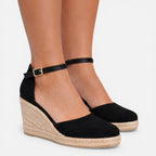 Closeup of a woman's ankles wearing black espadrille wedges with ankle strap and jute-wrapped heel