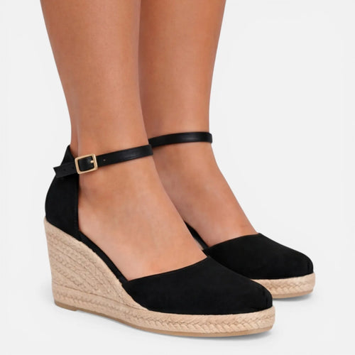 Closeup of a woman's ankles wearing black espadrille wedges with ankle strap and jute-wrapped heel