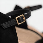 Macro detail of the gold buckle and black ankle strap on a closed-toe espadrille wedge