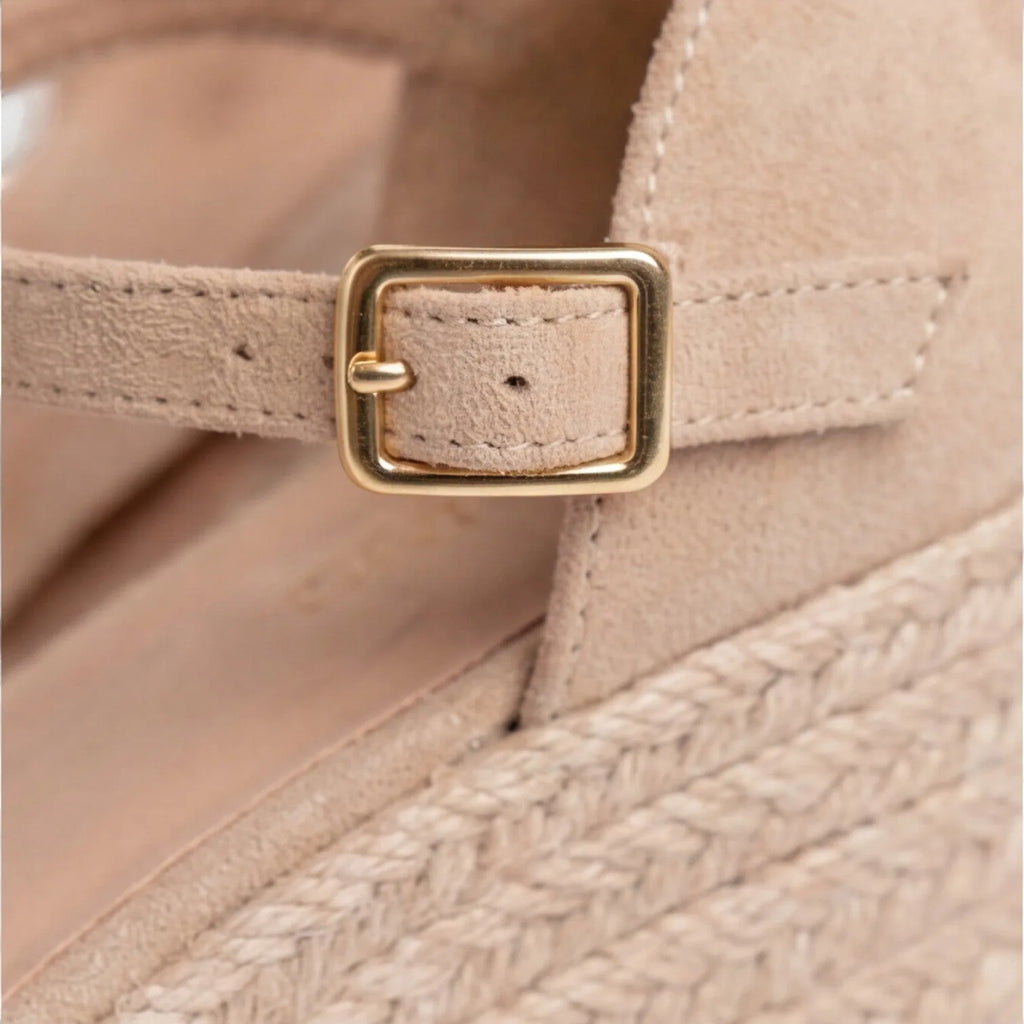 Macro detail of the gold buckle and beige suede strap against the jute wedge platform