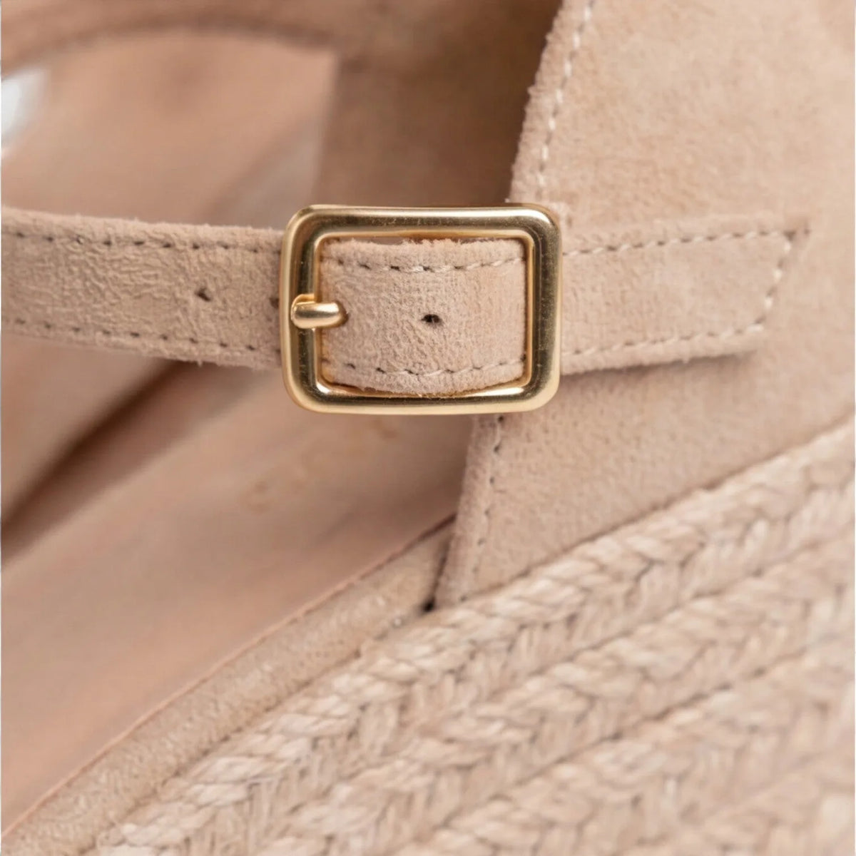 Macro detail of the gold buckle and beige suede strap against the jute wedge platform