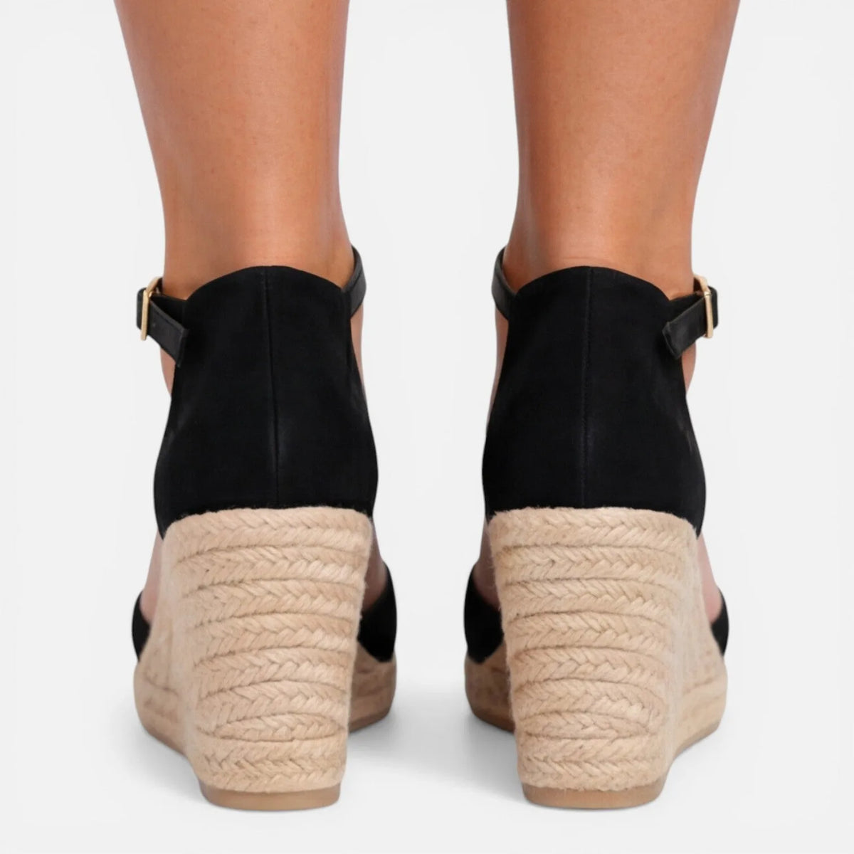 Back view of feet in black espadrille wedges showing the jute-wrapped heel and ankle buckles