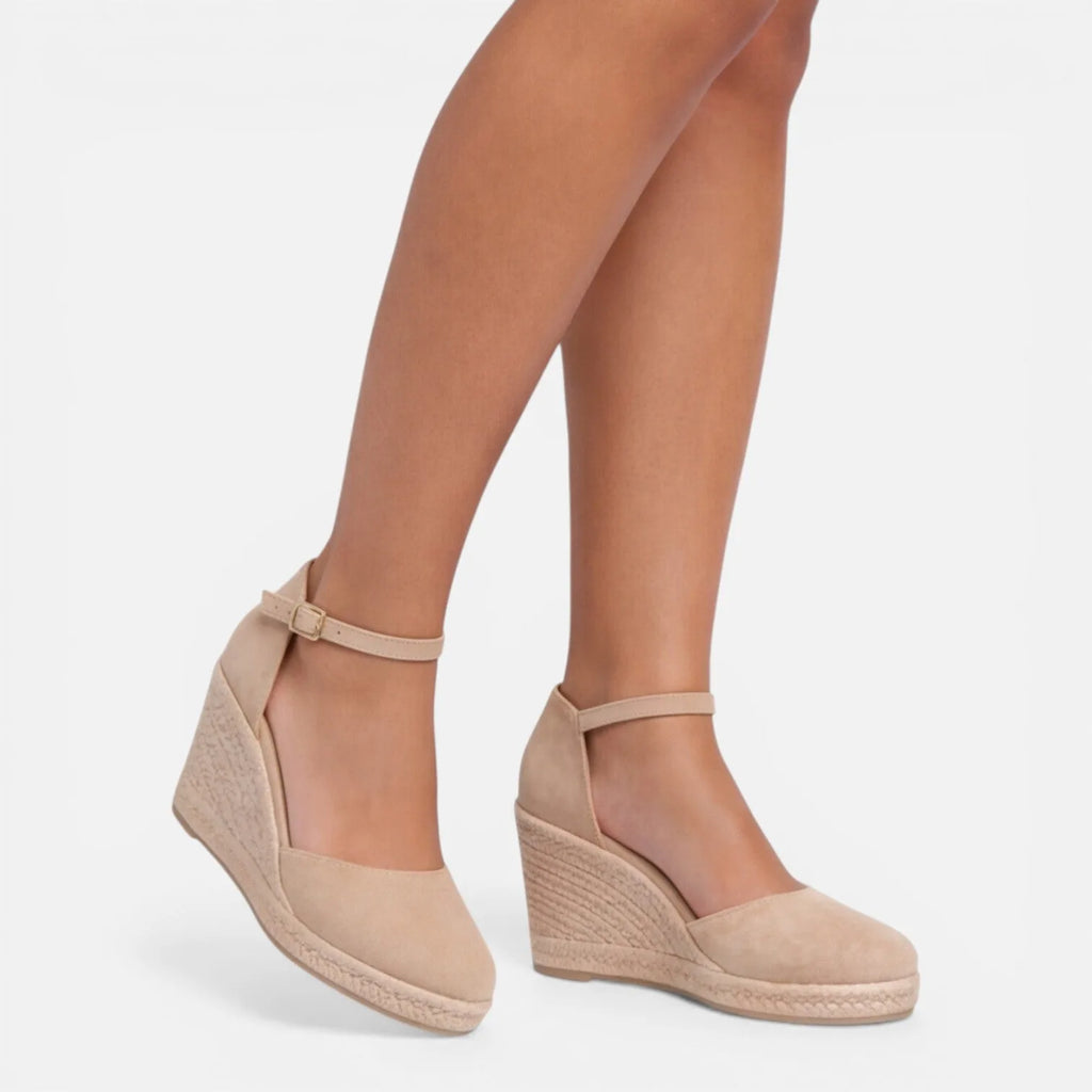 Side profile of a beige closed-toe espadrille wedge sandal with ankle strap on a model's foot