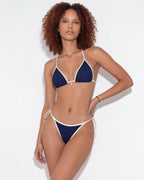 Front view of model wearing a navy triangle bikini with white contrast binding and gold charm detail