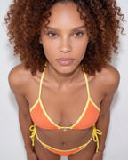 Model wearing navy bikini top with visible stitching detail along the cream binding
