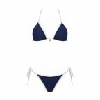 Flat lay of navy triangle bikini top and tie-side bottoms with cream piping and gold charm