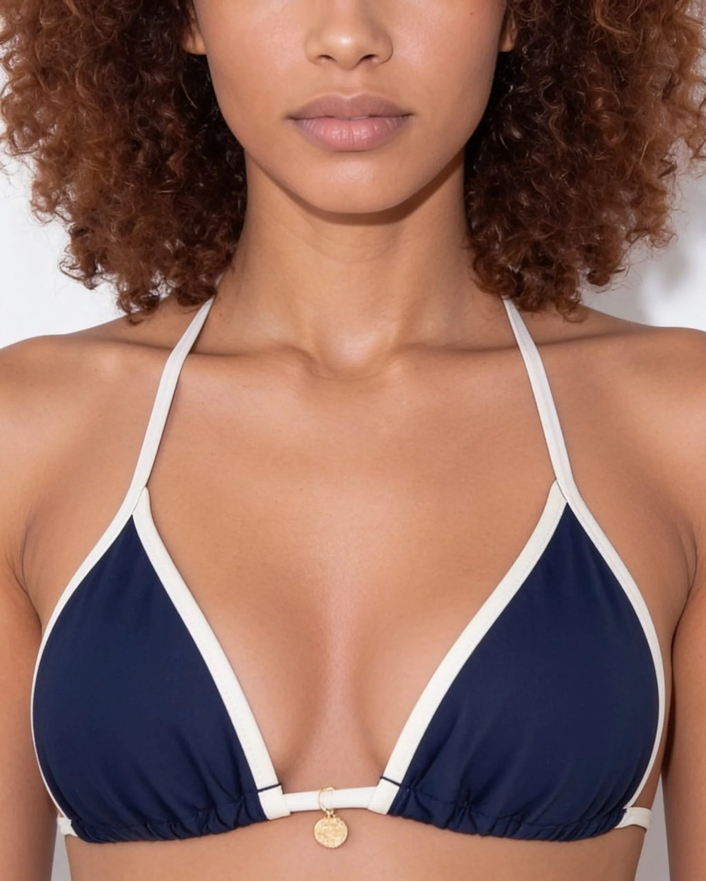 Close-up of navy triangle bikini top neckline showing cream binding and small gold charm pendant