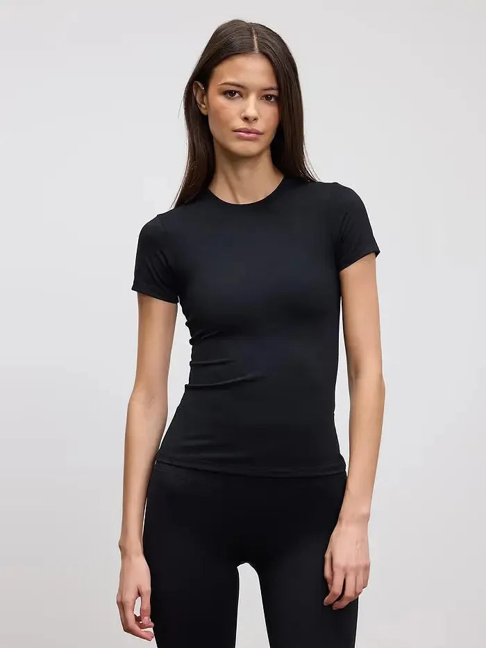 Woman modelling a fitted black crew neck tee with matching black leggings, plain studio background