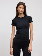 Woman modelling a fitted black crew neck tee with matching black leggings, plain studio background