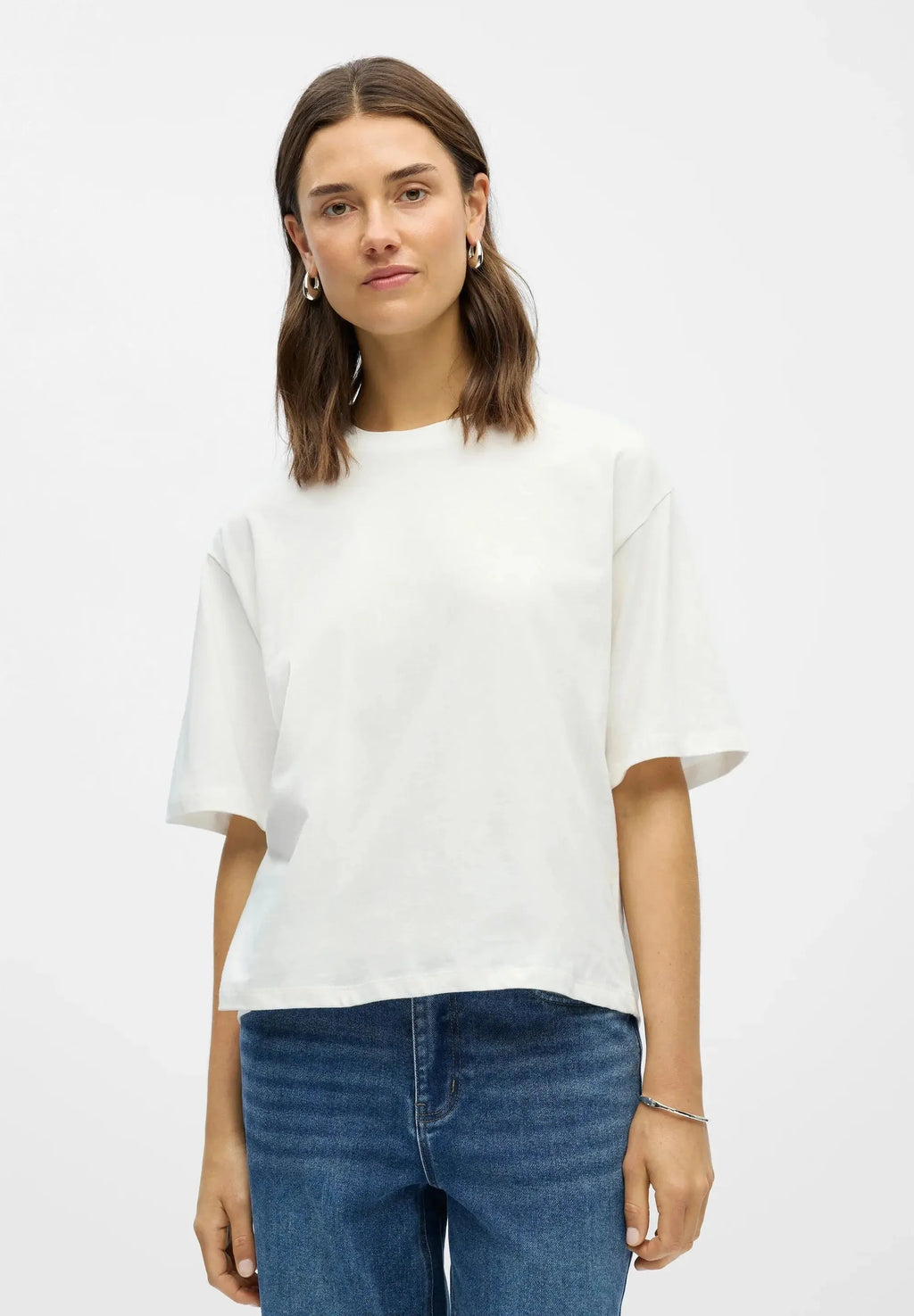 Relaxed boxy white cotton tee worn loose with blue denim jeans, front view with model wearing hoop earrings