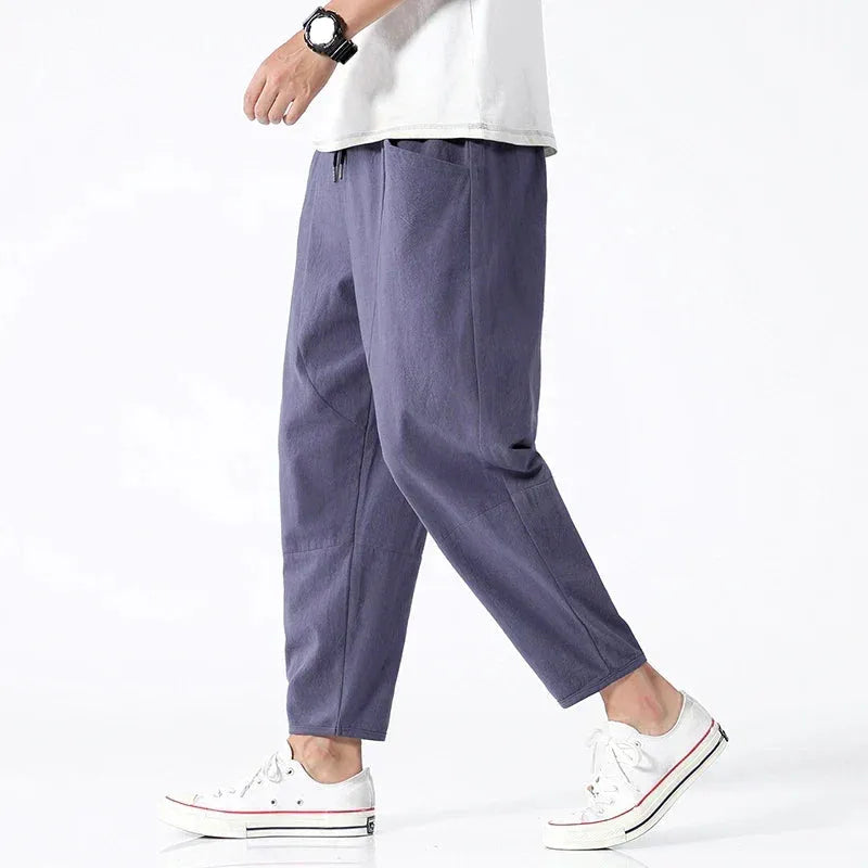 Side view of model walking in slate blue-grey cropped linen pants paired with a white t-shirt and white sneakers
