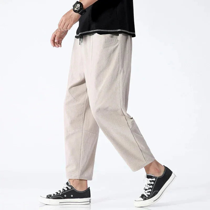 Model walking in beige cropped linen pants styled with a black t-shirt and black canvas sneakers