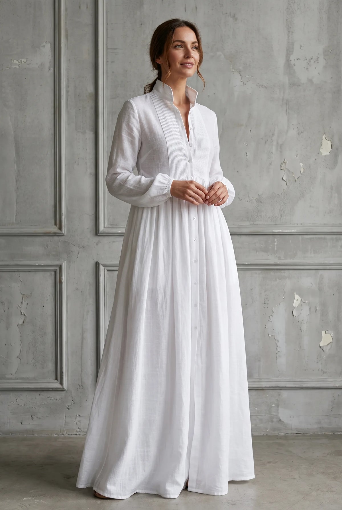Front view of a model in a white cotton linen maxi dress with stand-up collar, pintucked bib and button-through front.