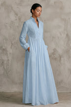 Side profile of a model in a pale blue cotton linen maxi dress with stand collar, hands resting in the side pockets.