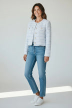 Woman wearing a cropped powder blue boucle jacket with pearl buttons over jeans and a white tee, front view.