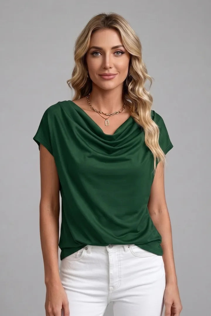 Woman modelling the dark green cowl neck top with draped front detail, paired with white jeans
