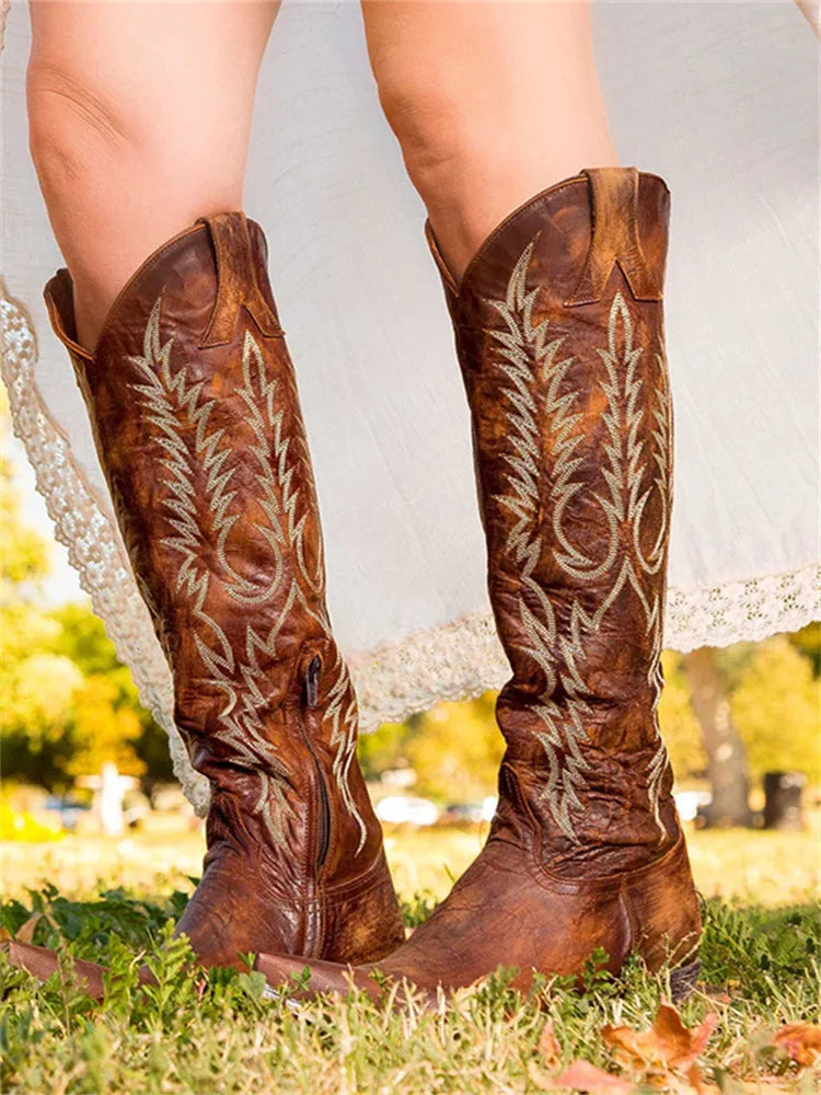 Back view of brown leather knee-high western boots with cream embroidery and low stacked heel, worn with a flowing dress