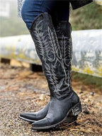 Side profile of black distressed leather knee-high cowboy boots showing pointed toe and tonal embroidered stitching