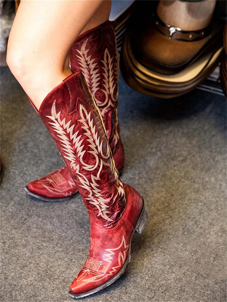 Close-up side view of red leather knee-high western boots with intricate cream embroidery and pull tab detail