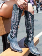 Seated view of blue-grey distressed leather knee-high cowboy boots showing contrast stitching and slouch shaft