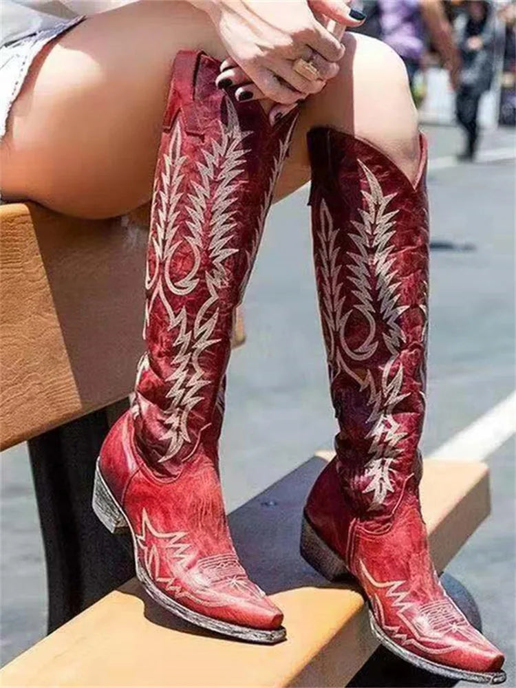 Crossed-leg view of red leather knee-high cowboy boots showing worn sole and low block heel detail