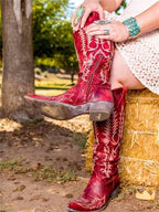 Close-up of red leather knee-high boots with side zip and cream stitching, styled with turquoise jewellery