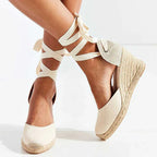 Close-up of white canvas espadrille wedge sandal with woven jute wedge and cream ankle-tie laces crossed up the leg