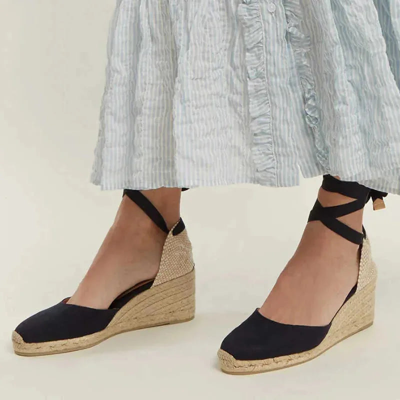 Close-up of black canvas espadrille wedge sandals with jute wrap sole and ankle ties, paired with a striped midi skirt