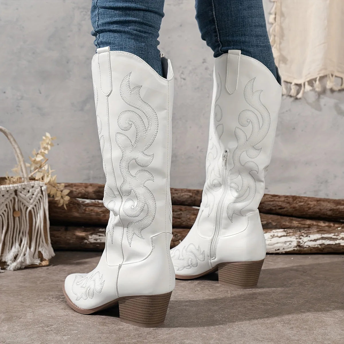 Back view of white knee-high cowboy boots with scroll embroidery and a stacked block heel, worn with skinny jeans