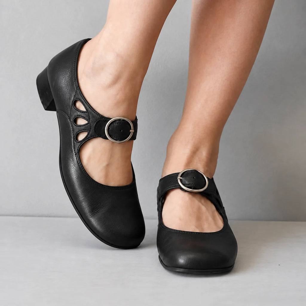 Side view of black leather mary jane flats with teardrop cutouts and a round silver buckle strap on the ankle