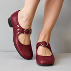 Burgundy leather mary jane flats with cutout ankle strap and silver buckle, shown worn with legs crossed
