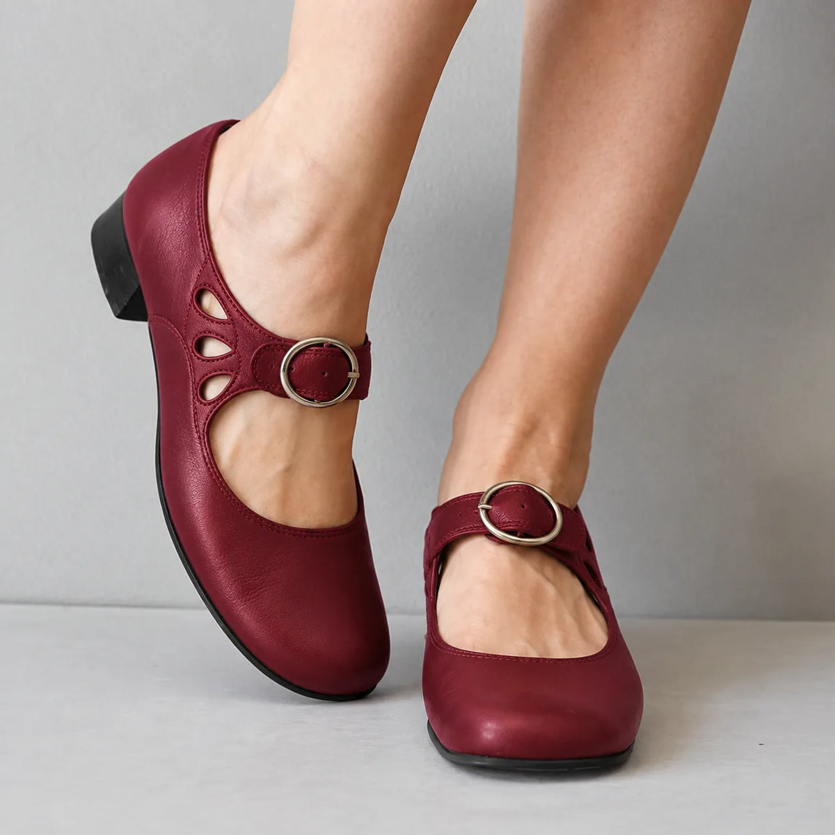 Burgundy leather mary jane flats with cutout ankle strap and silver buckle, shown worn with legs crossed