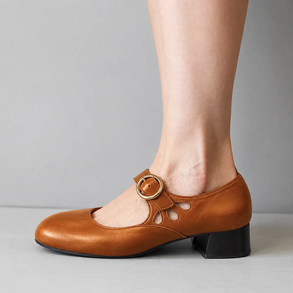 Close side profile of a tan leather mary jane flat showing the round gold buckle and low stacked heel