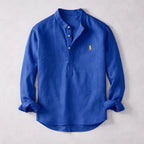 Royal blue henley shirt with stand collar and contrast embroidered logo, sleeves rolled, laid flat on grey