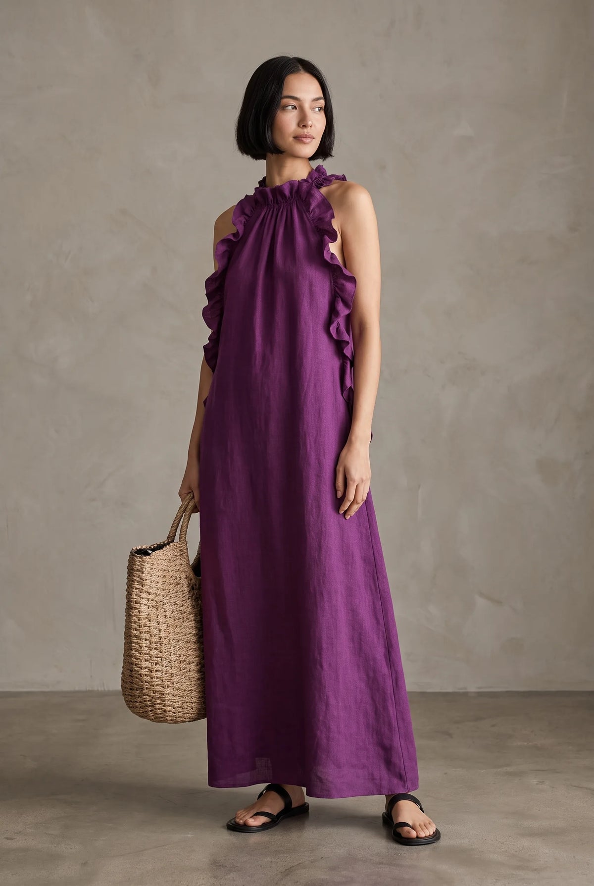 Model in a purple linen halter maxi dress with ruffled neckline detail, carrying a natural woven tote bag