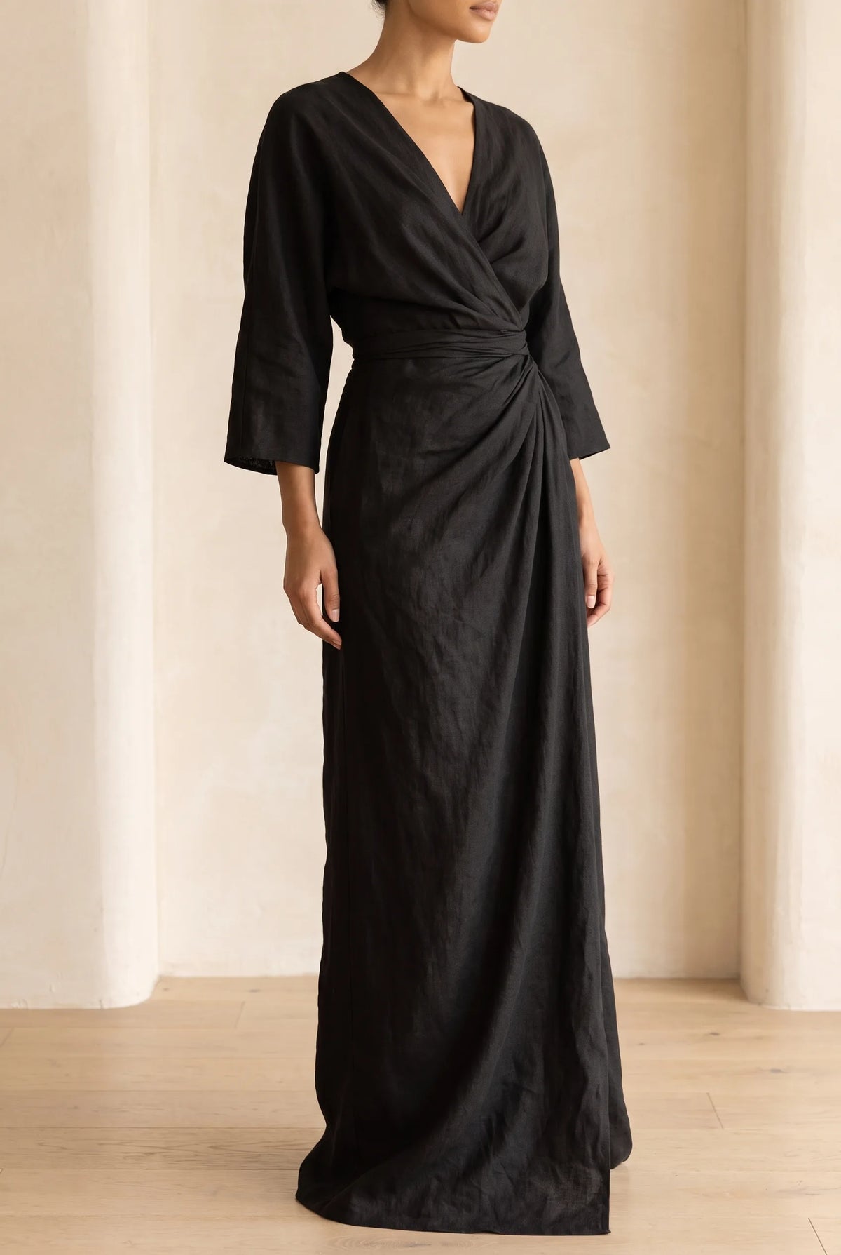 Side view of the dress in black, showing the wrap V-neckline, gathered waist and long sleeves against a plain backdrop